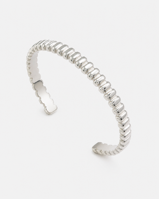 Offener silberfarbener Edelstahl-Cuff Armreif mit geriffelter, moderner Struktur auf hellem Hintergrund.