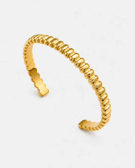 Offener vergoldeter Edelstahl-Cuff Armreif mit geriffelter, moderner Struktur auf hellem Hintergrund.